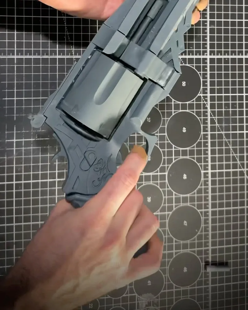 An unpainted grey test print of the Blue Rose revolver held on a cutting mat